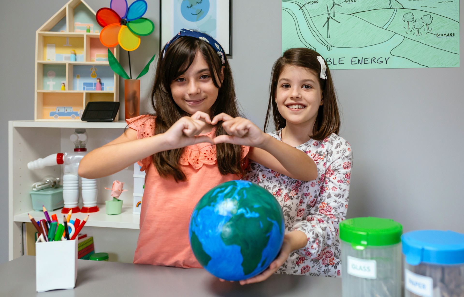 Two female students showing globe world earth while one making heart shape with hands