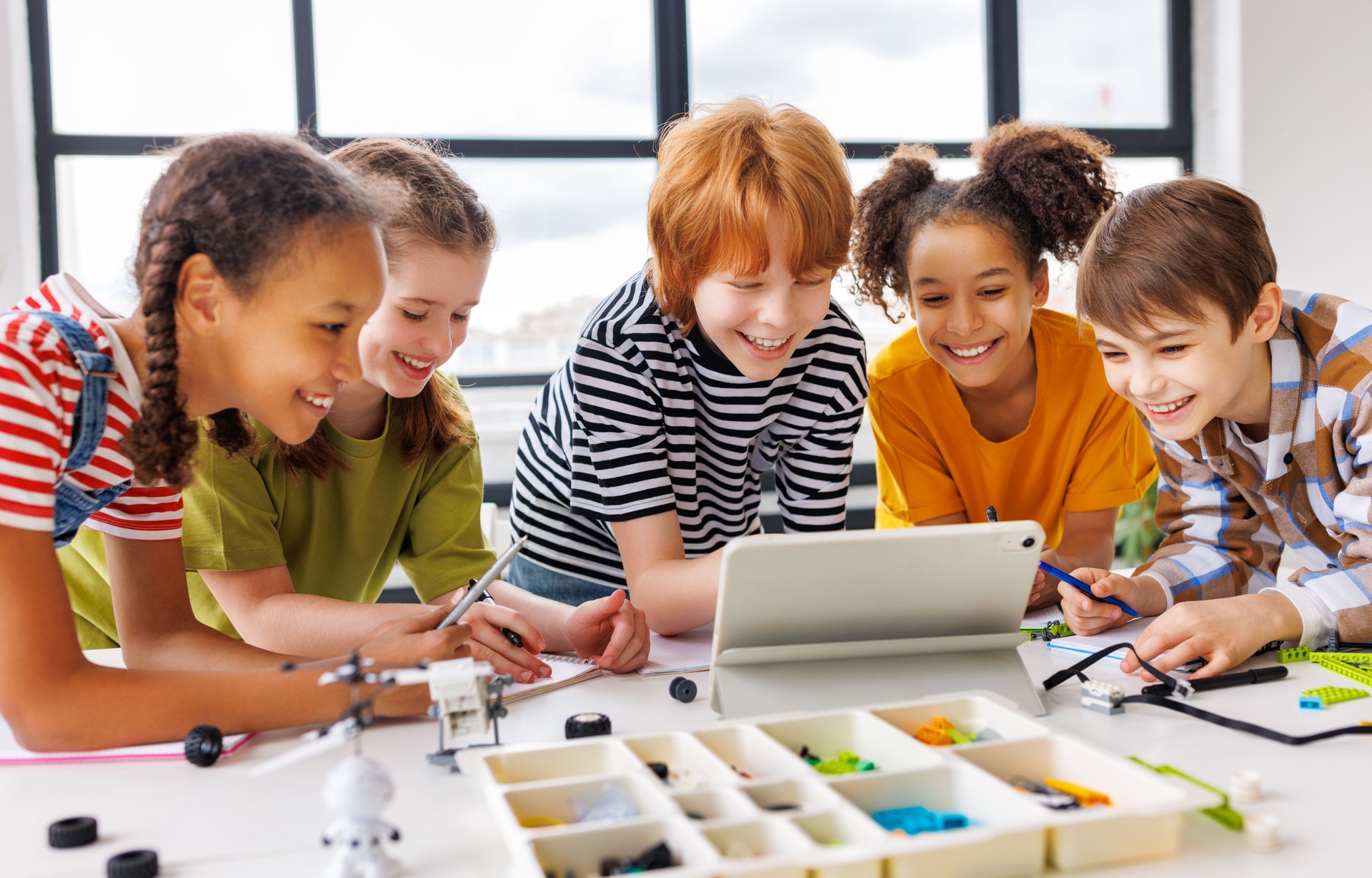 Cheerful  schoolkids   looking at tablet screen and study the scheme of assembly of robots during collective school work   during online lesson